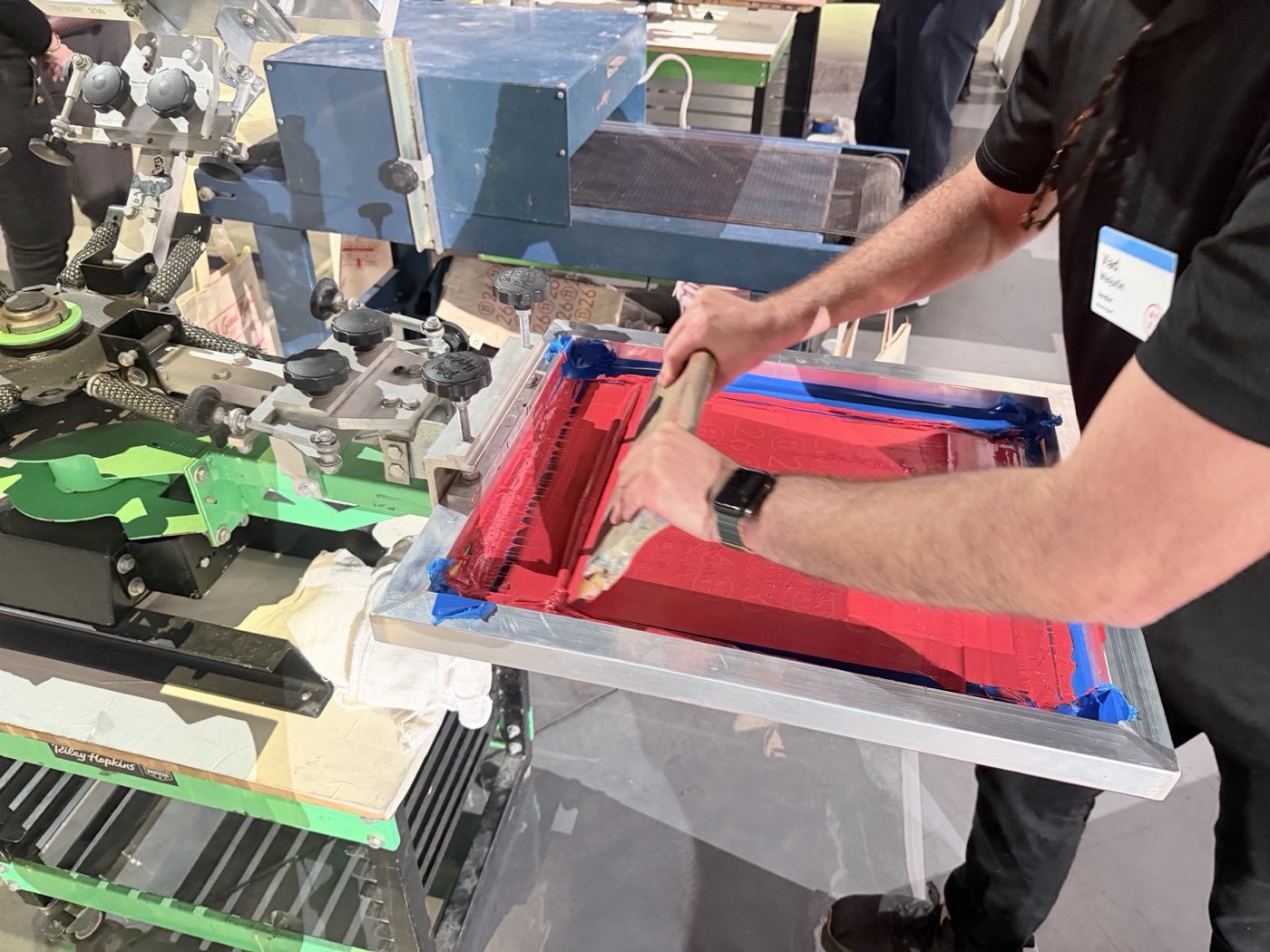 Print operator flooding red ink across a screen on a manual press at a live printing station